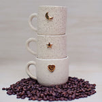 Celestial Mugs. These exquisite handmade ceramic coffee / tea mugs are adorned with real gold paint, adding a touch of luxury to your morning routine. Each unique mug features charming figures like hearts, moons, and stars, making them not only functional but also a delight to behold. Elevate your coffee experience with these beautifully crafted pieces.